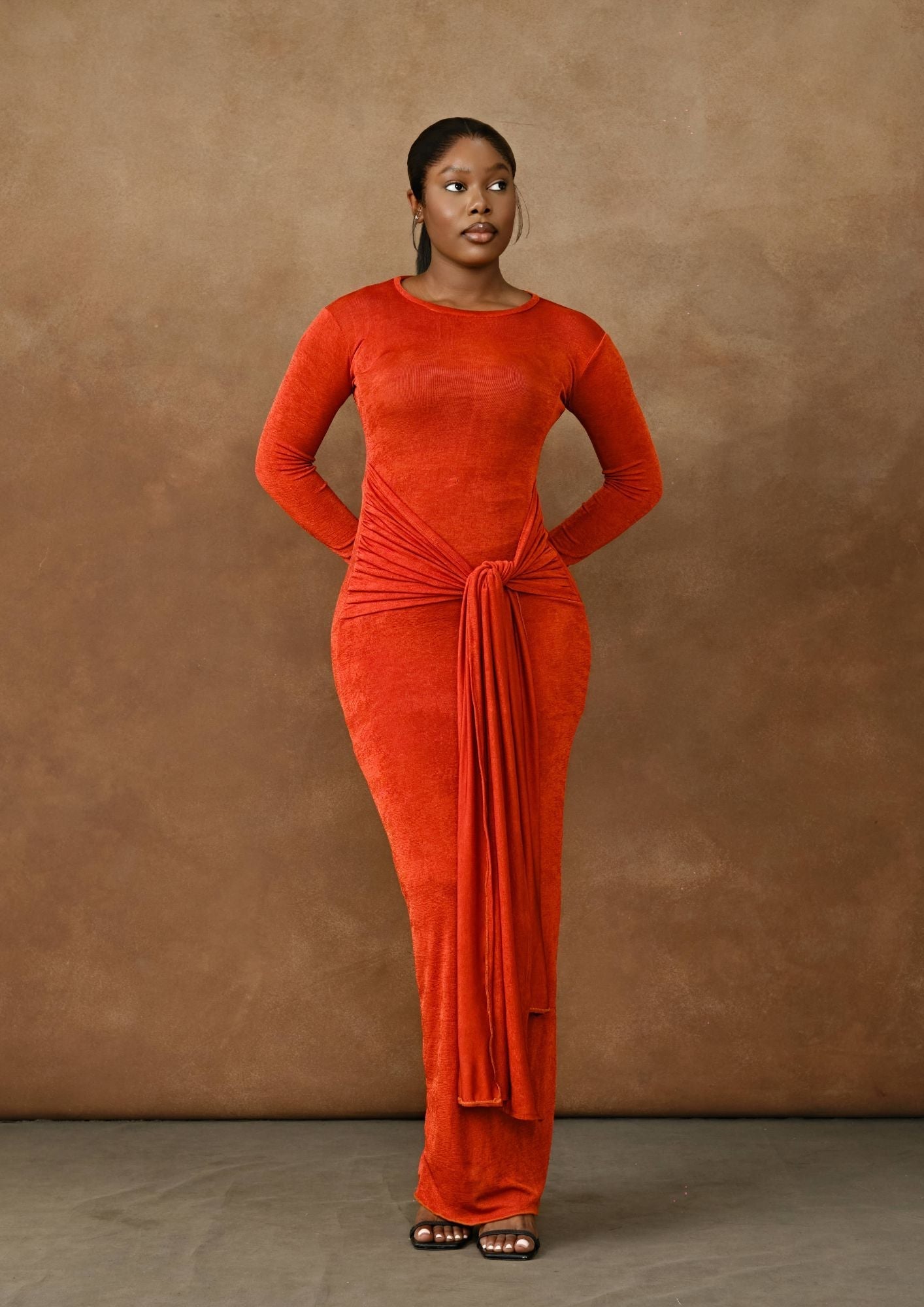 Woman in a fitted burnt orange long-sleeve gown with front drape detail, seamless background