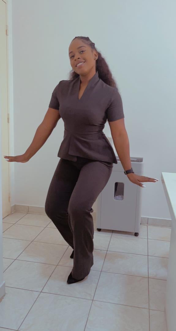 Woman in tailored brown pantsuit posing in a modern, minimalist workspace