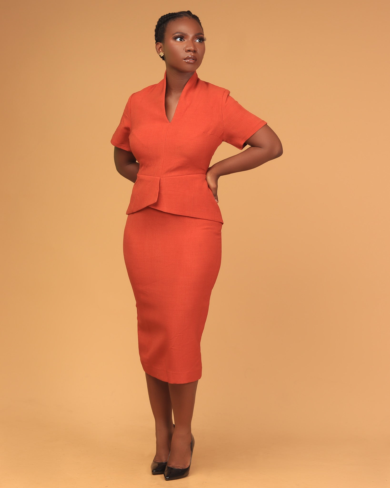 Woman in tailored orange skirt suit with short sleeves, standing against beige background